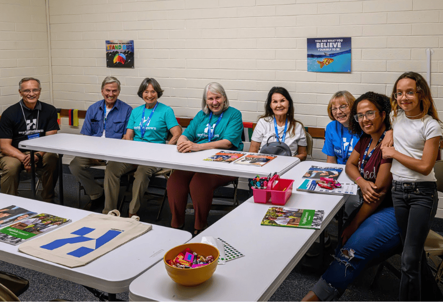Group of volunteers seated at tables with flyers and materials for a myHometown community outreach event