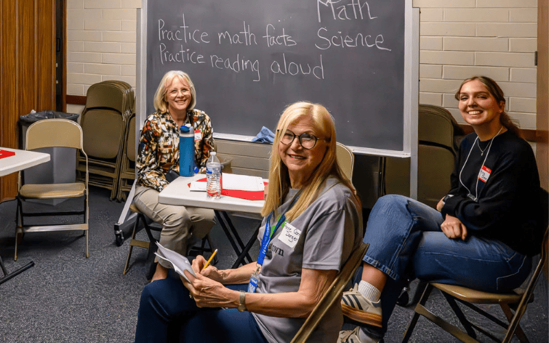 Smiling volunteers gathered in a classroom with notes and materials for tutoring and learning support