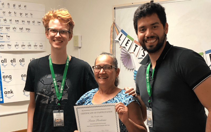 Adult learner holding a certificate with two volunteers celebrating completion of an educational program