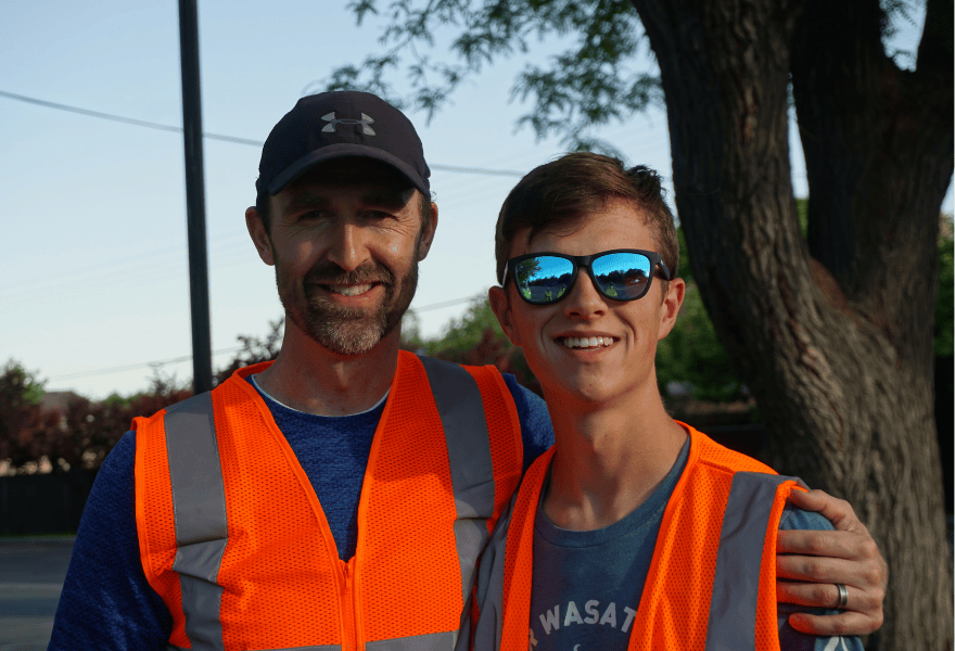 Adult and teen volunteer standing side by side in orange safety vests at an outdoor cleanup event