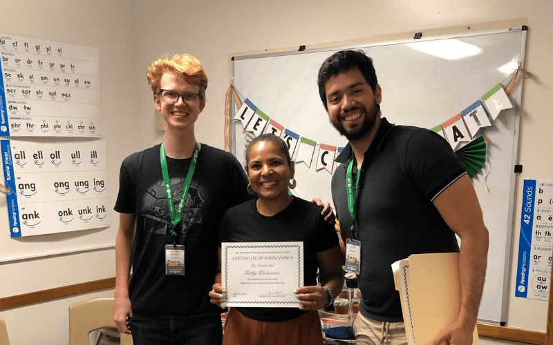 Program participant smiling with certificate alongside mentors in a classroom setting