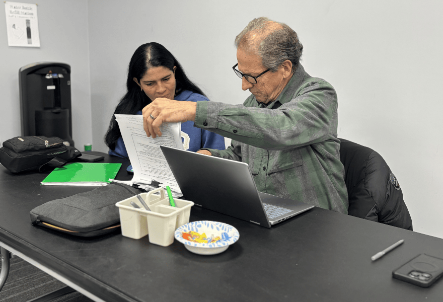 Volunteer helping a community member review paperwork at a laptop during a local community service program in Utah, supporting upward mobility and neighborhood assistance