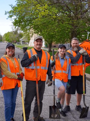 Four volunteers wearing safety vests and holding shovels while working together on a street cleanup project